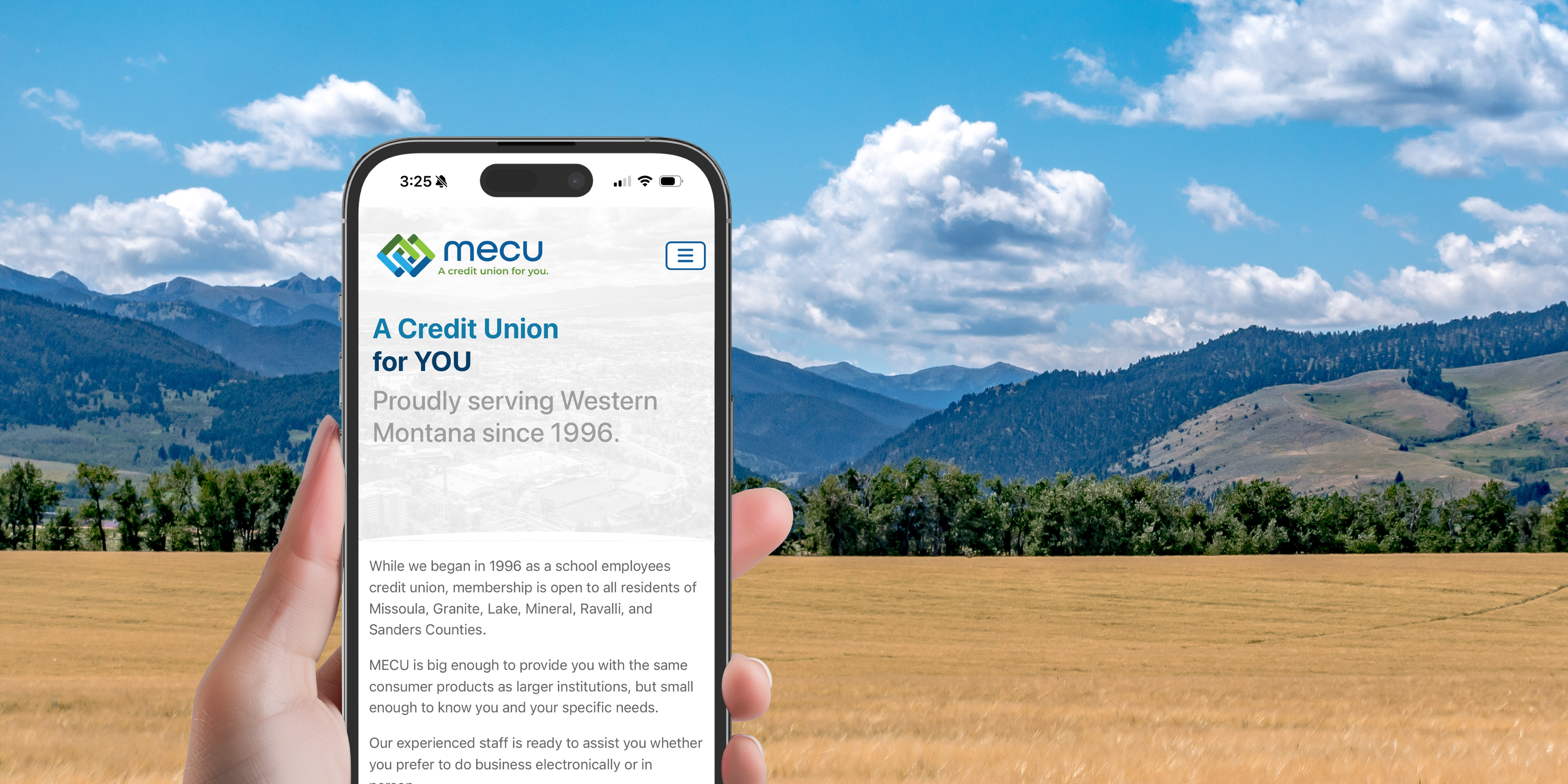 Image of hand holding a phone with the Montana Educators Credit Union website pulled up with a mountain background
