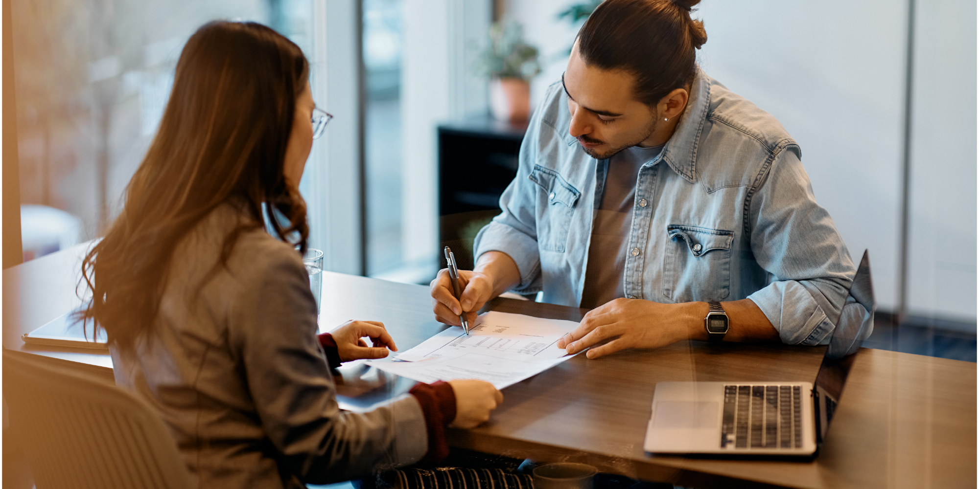 Image shows man signing form across table from woman in a bank setting